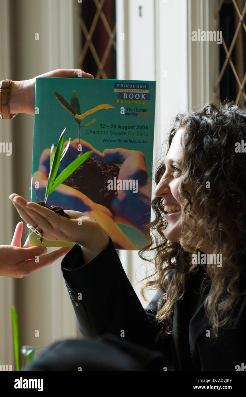 Giovane donna in possesso di una pianta crescente nel suo palm, mimando l'immagine sul libro dietro. Foto Stock