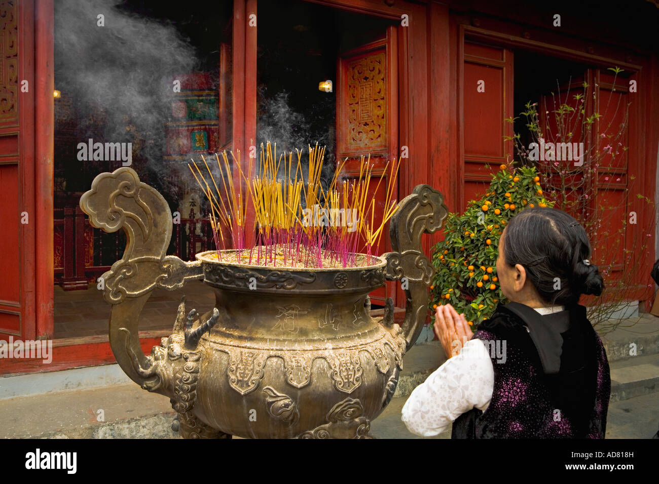 Incenso diffondendo una donna di preghiera verso la porta aperta del 'Ngoc Son Pagoda', Hanoi. Foto Stock