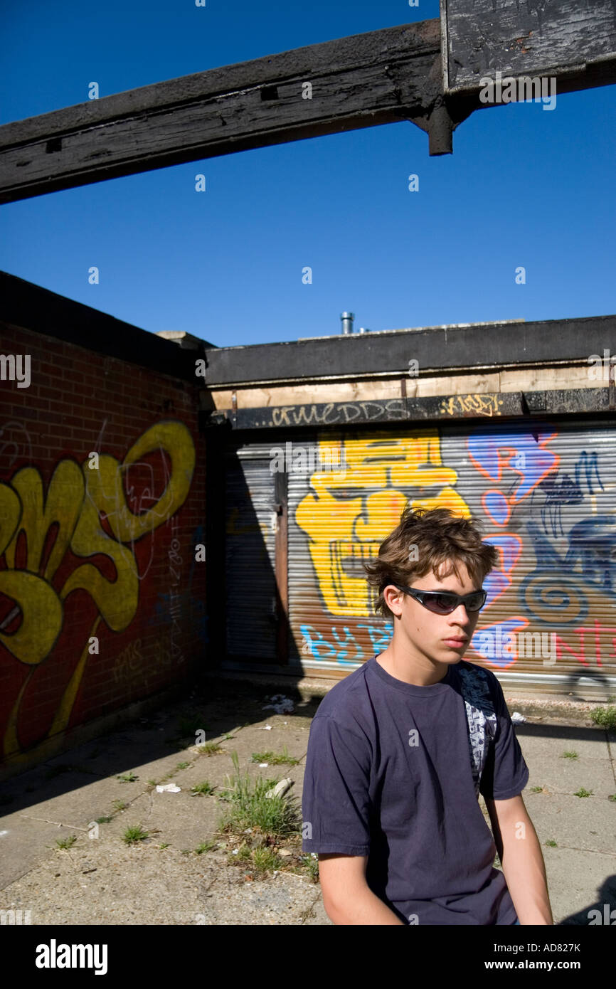 Ragazzo adolescente indossando occhiali da sole seduto fuori da un edificio coperto di graffiti colorati Foto Stock