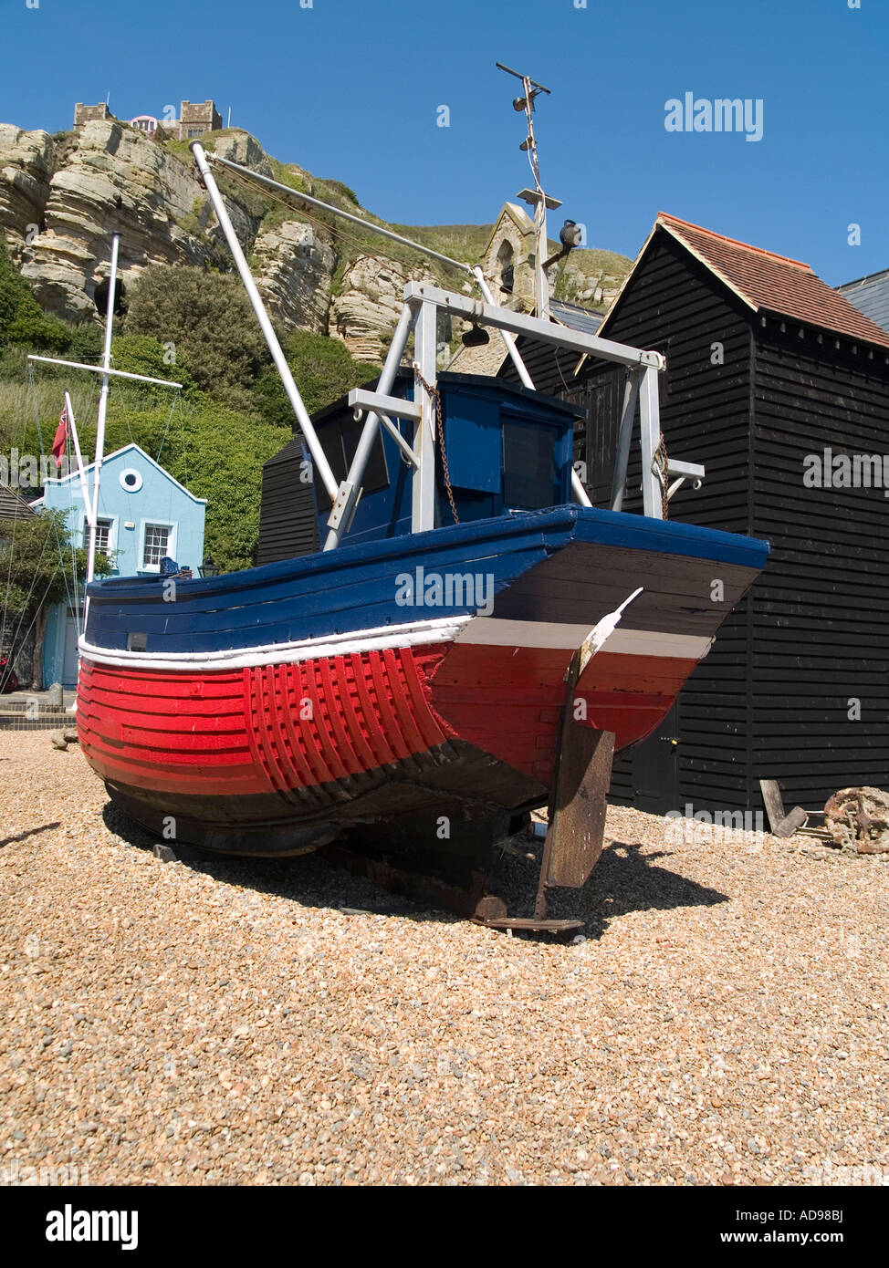 Un tradizionale di rosso e di blu dipinto di barca da pesca al di fuori del centro storico di capanne in legno per lo storage di rete East Cliff Hastings Regno Unito Foto Stock