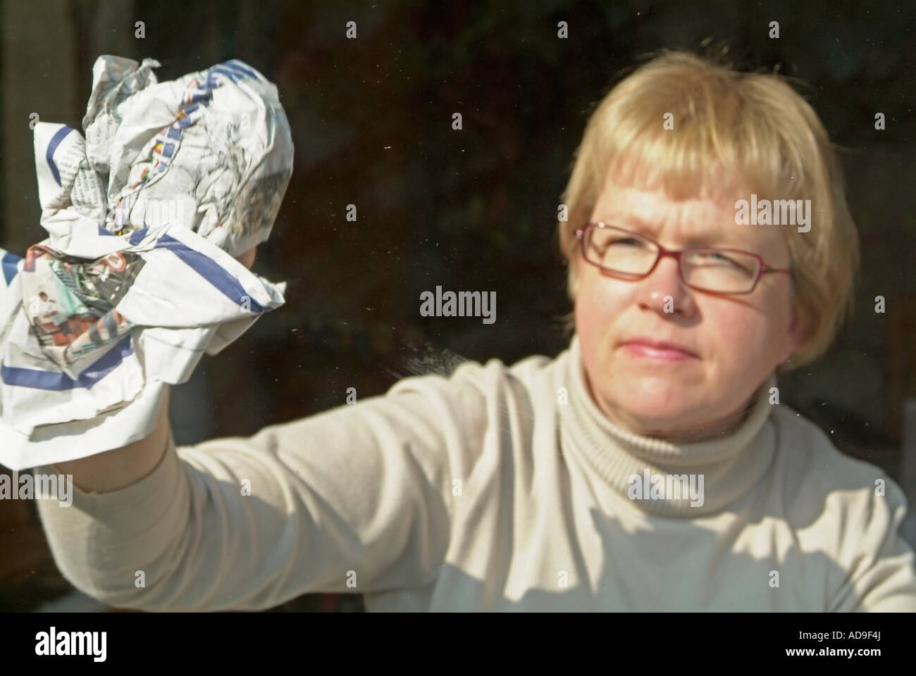 Donna di pulizia lucidatura finestra di vetro con quotidiano Foto Stock