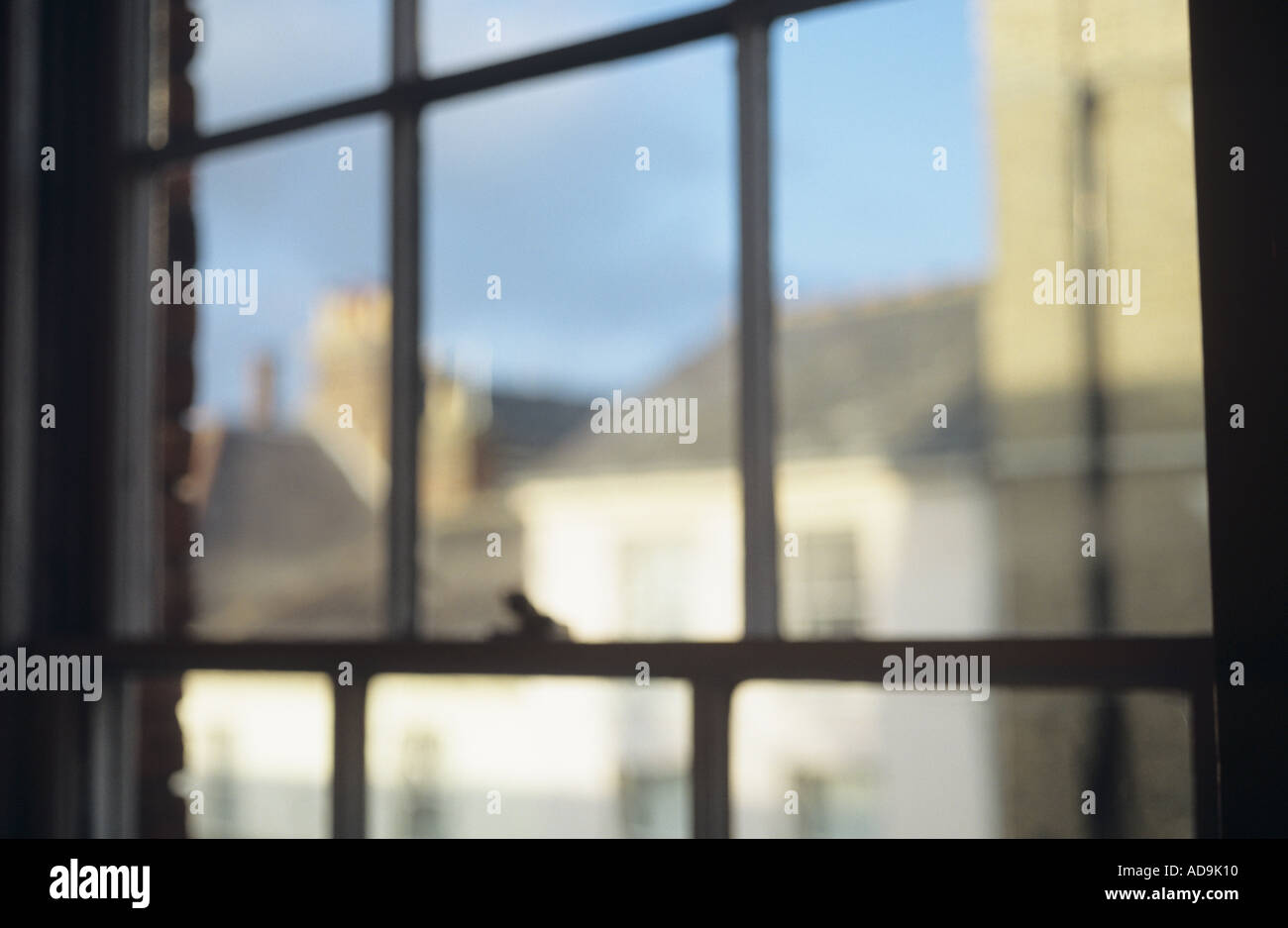Impressionistica vista attraverso uno stile Regency finestre a ghigliottina verso townhouses sui tetti della città e camini sotto il cielo blu Foto Stock