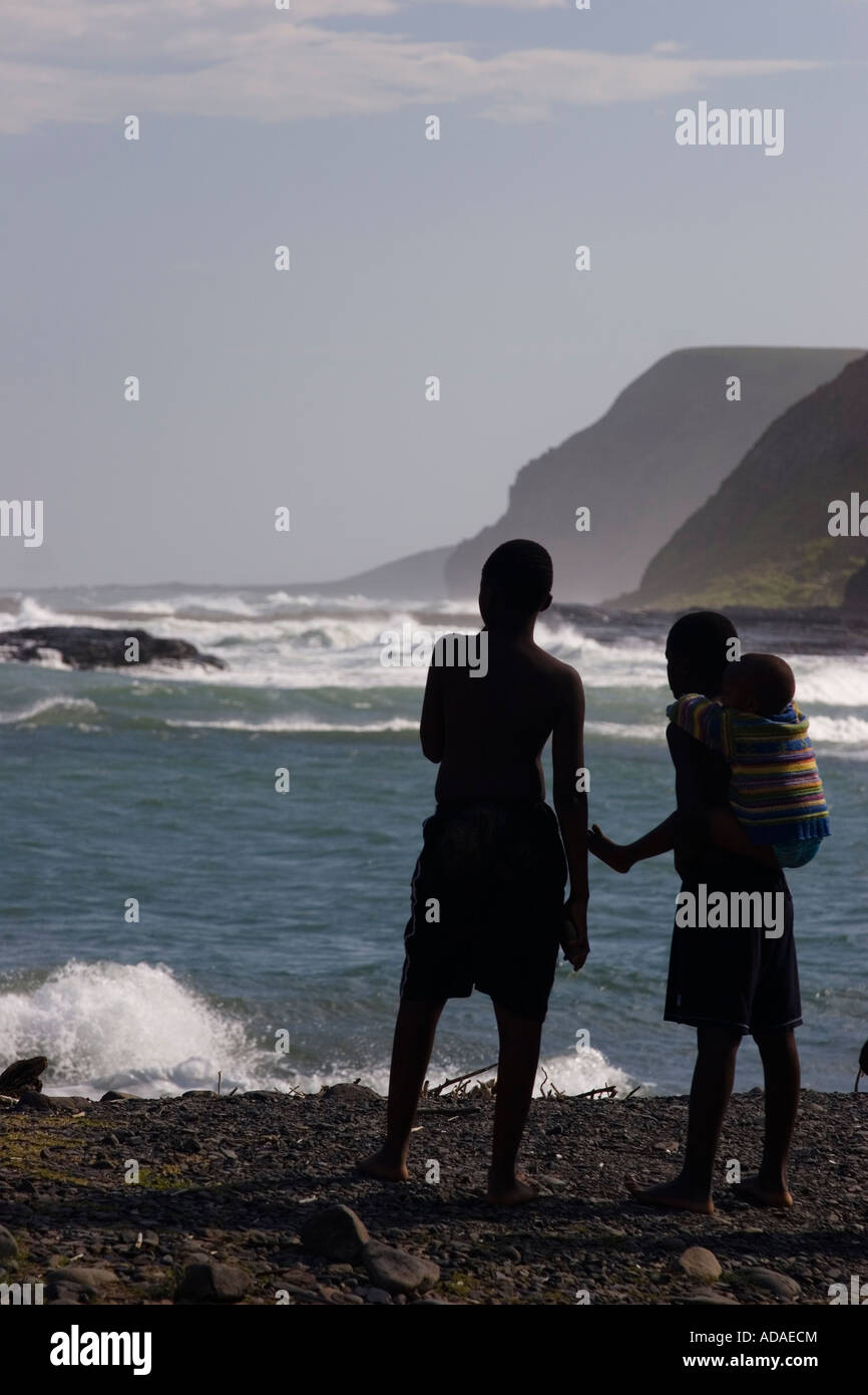 Bambino africano seduto sul retro del suo fratello a 'buco nel muro" e guarda l'oceano, Transkei, Sud Africa Foto Stock
