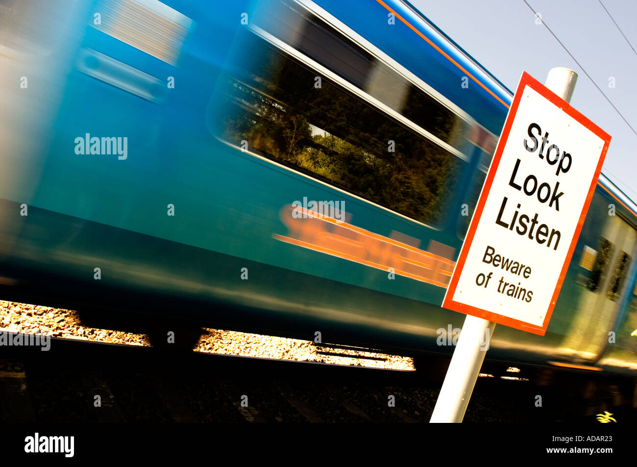 Treno accelerando attraverso una rampa pedonale incrocio con segnale di avvertimento Foto Stock