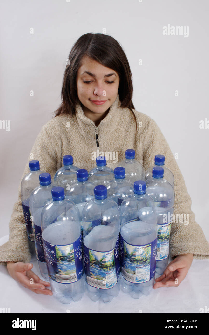 Ragazza adolescente/giovane donna in giacca di lana in posa con 12 di plastica di bottiglie di acqua Foto Stock