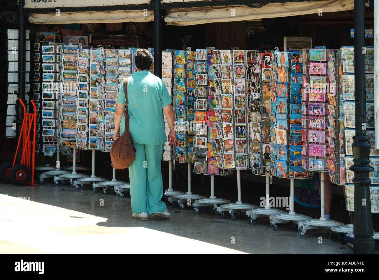 Cliente St Tropez negozio di souvenir una donna che guarda la visione & acquisto all'esterno esposizione di cartoline & biglietti d'auguri su Spinner rack sud della Francia Foto Stock