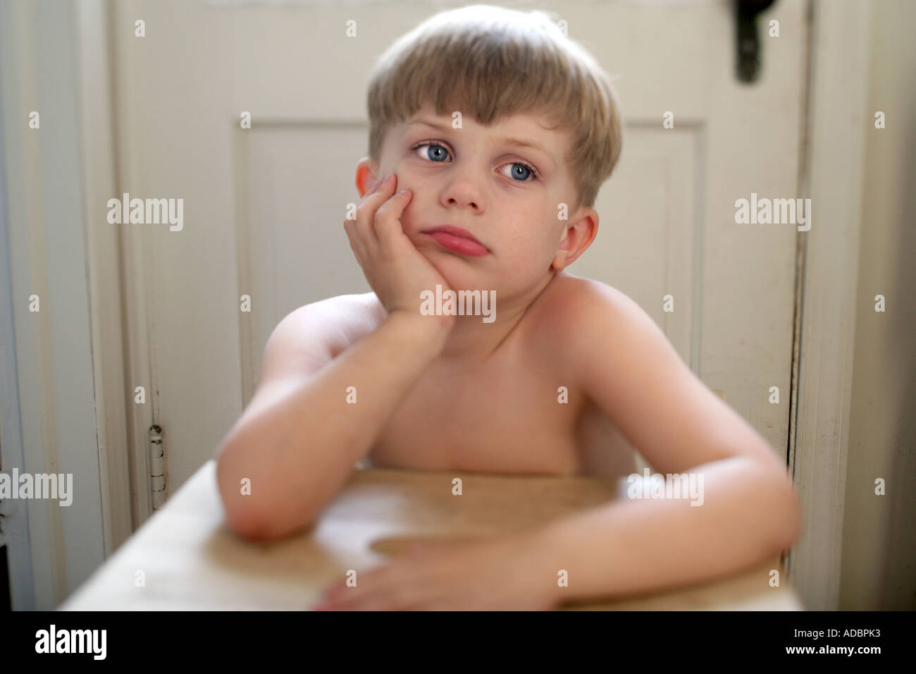 Un annoiato bambino seduto al tavolino cercando infelice e premuto Foto Stock