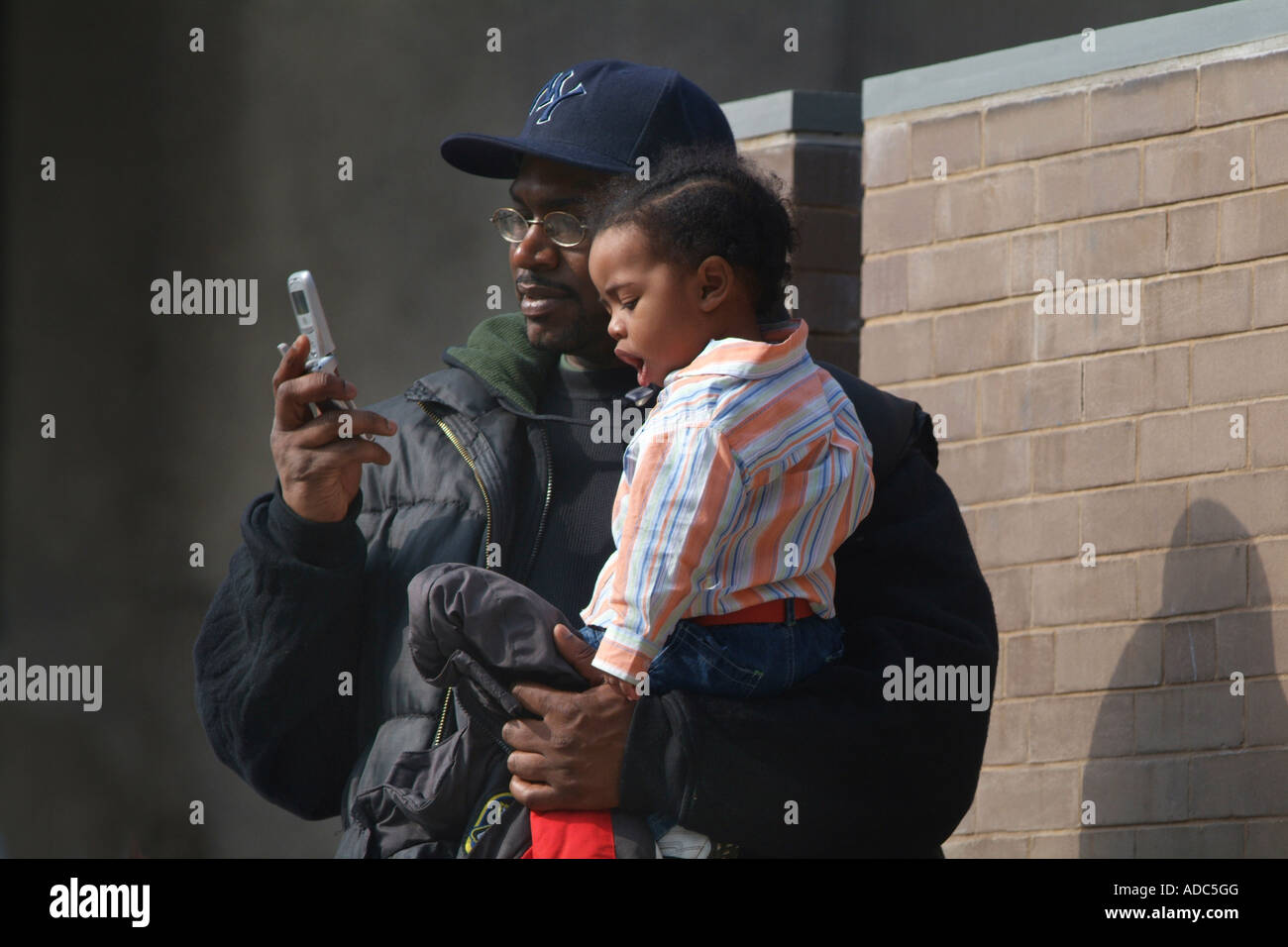 Un uomo invia un messaggio di testo utilizzando un telefono cellulare mantenendo la sua giovane figlia Foto Stock