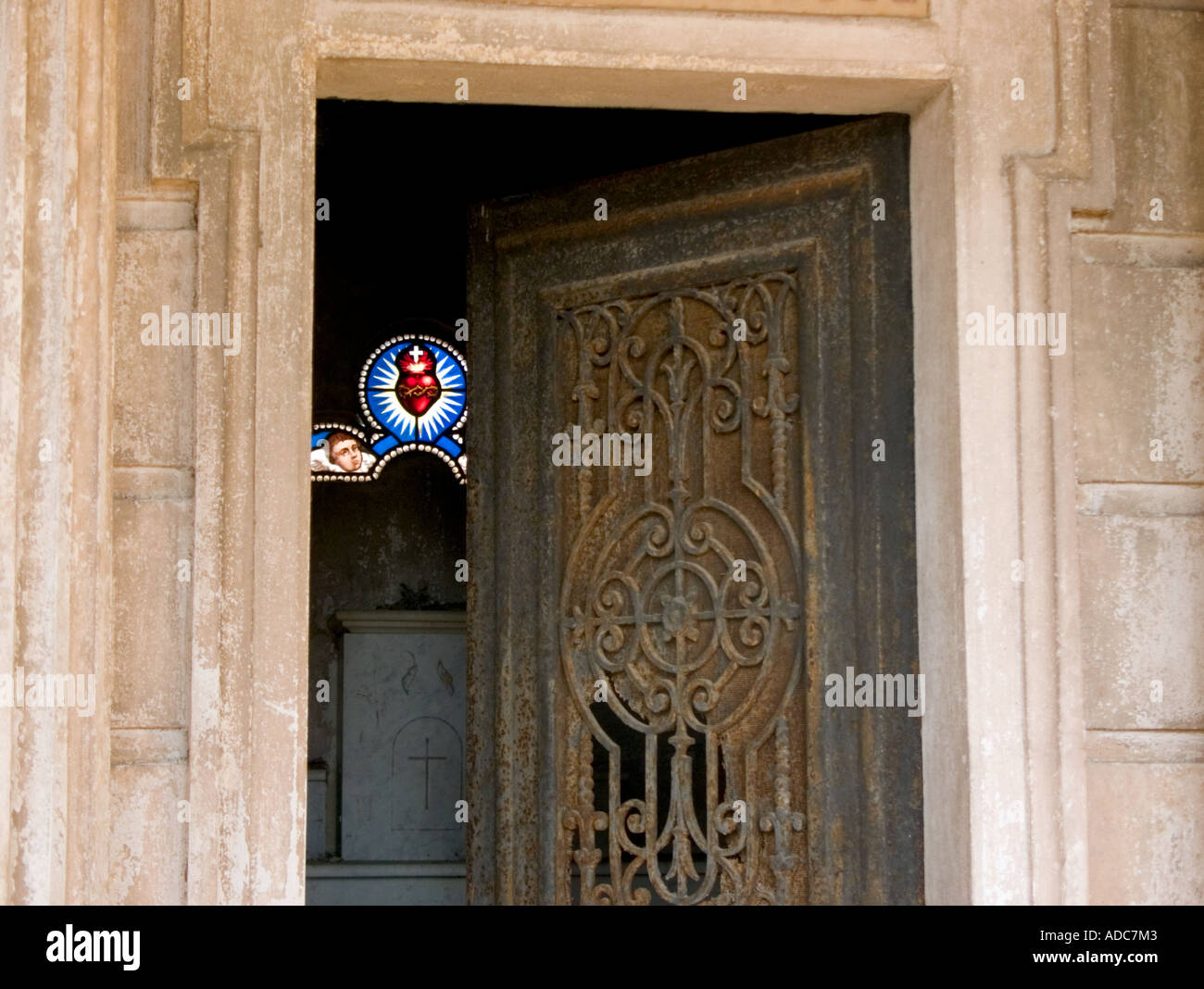 Una vista attraverso un aperto il ferro battuto porta a macchia finestra vetrate di cuore e di Angelo nella tomba Foto Stock