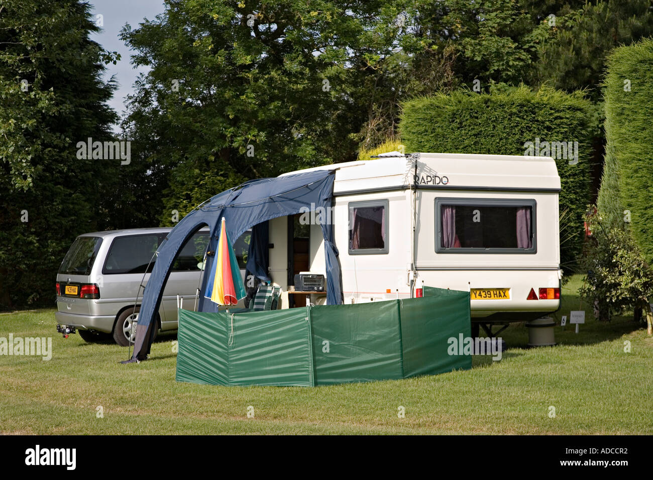 Caravan inclinate con tenda da sole e frangivento con auto parcheggiate a fianco in un campeggio su Anglesey nel Galles del Nord Regno Unito Foto Stock