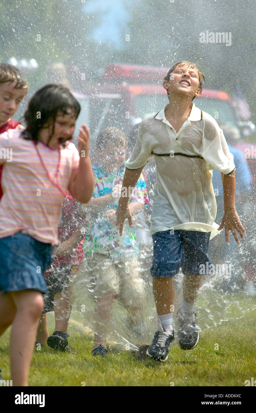 Giovani salto attraverso il modello Firehose di spruzzare alla piccola città del 4 luglio festa Foto Stock