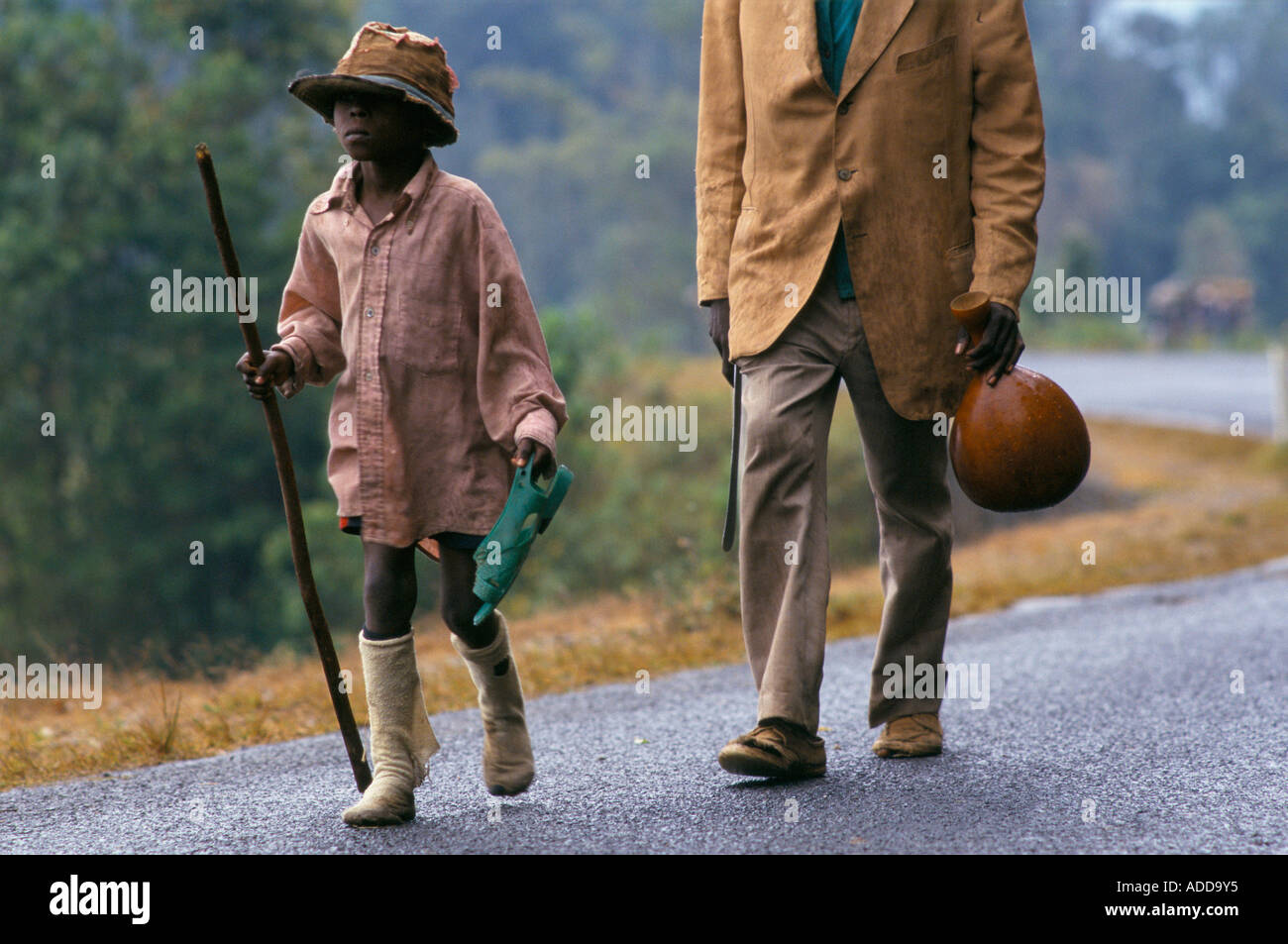 Un giovane bambino tiene un sandalo verde e un bastone come egli cammina verso la frontiera zairese di Bukavu. Foto Stock