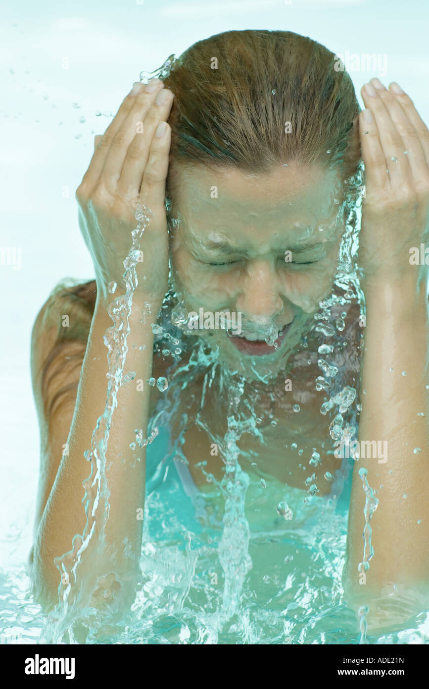 Giovane donna in piscina, schizzi viso con acqua Foto Stock