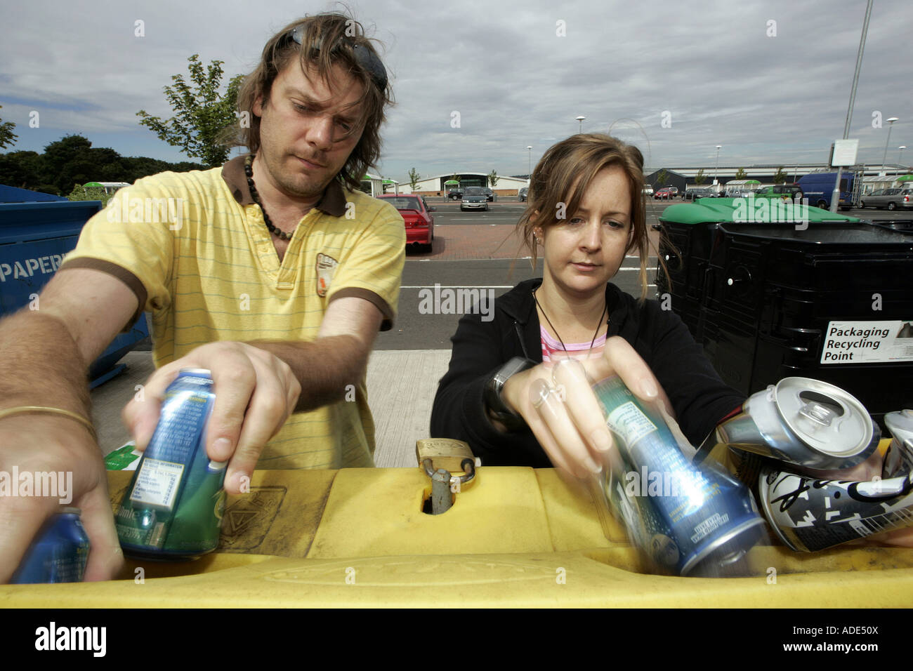 Una giovane coppia il riciclo dei barattoli di alluminio in un supermercato area di riciclaggio. Foto Stock