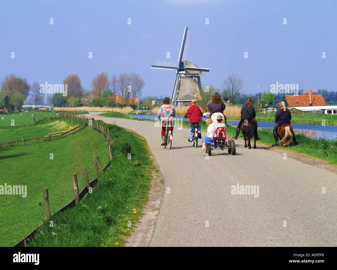 Equitazione per bambini di carretti e pony e biciclette sul rurale elevata canal road in Olanda ultimi mulini a vento e fattorie Foto Stock