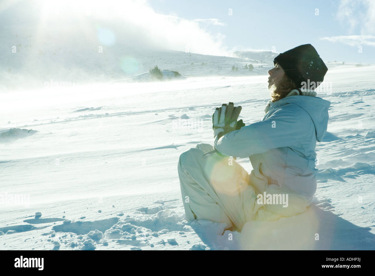 Teen ragazza seduta nella neve con le mani incrociate e gli occhi chiusi Foto Stock