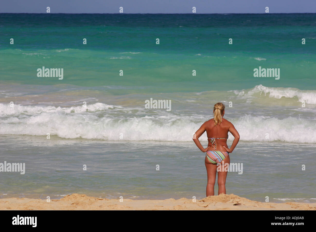 La mezza età della donna in bikini permanente sulla spiaggia per guardare oceano con torna alla fotocamera Foto Stock