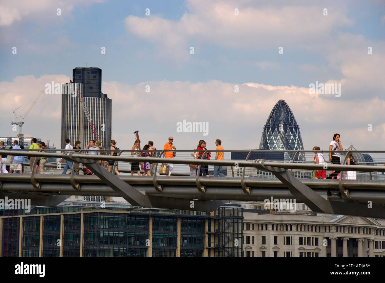 La gente camminare sopra il Millennium Bridge di Londra Tower 42 e il Gherkin edifici sono in background Foto Stock
