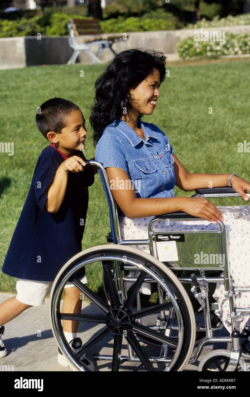 Ragazzo giovane spingendo la mamma in sedia a rotelle. volontario multi inter etniche della diversità razziale razziale multiculturale interracial culturale di minoranza Foto Stock