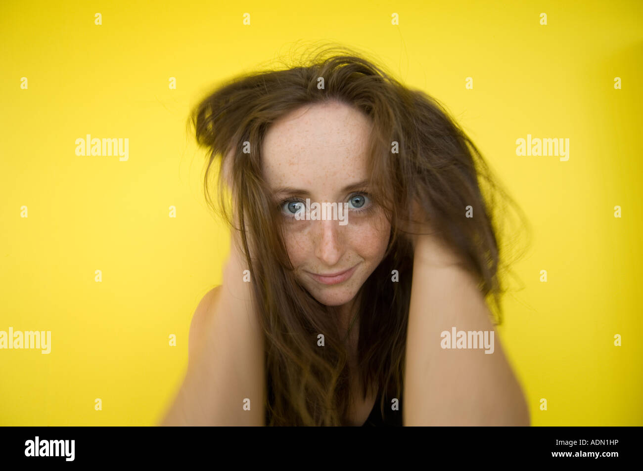 Wild cercando crazy dai capelli rossi redhead freckle face donna con in mano i suoi capelli fissando la telecamera contro sfondo giallo Foto Stock