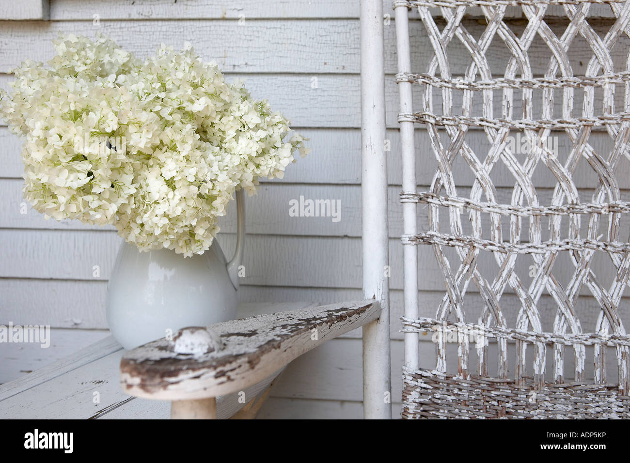 White ortensie in brocca sulla parte anteriore portico con sedia a dondolo Foto Stock