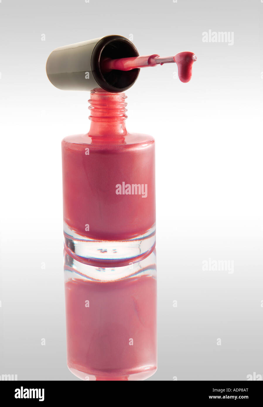 Smalto per unghie gocciolare da un smalto per unghie Spazzolino equilibrata su un chiodo del vaso di vernice rosa contro di colore bianco con una riflessione Foto Stock
