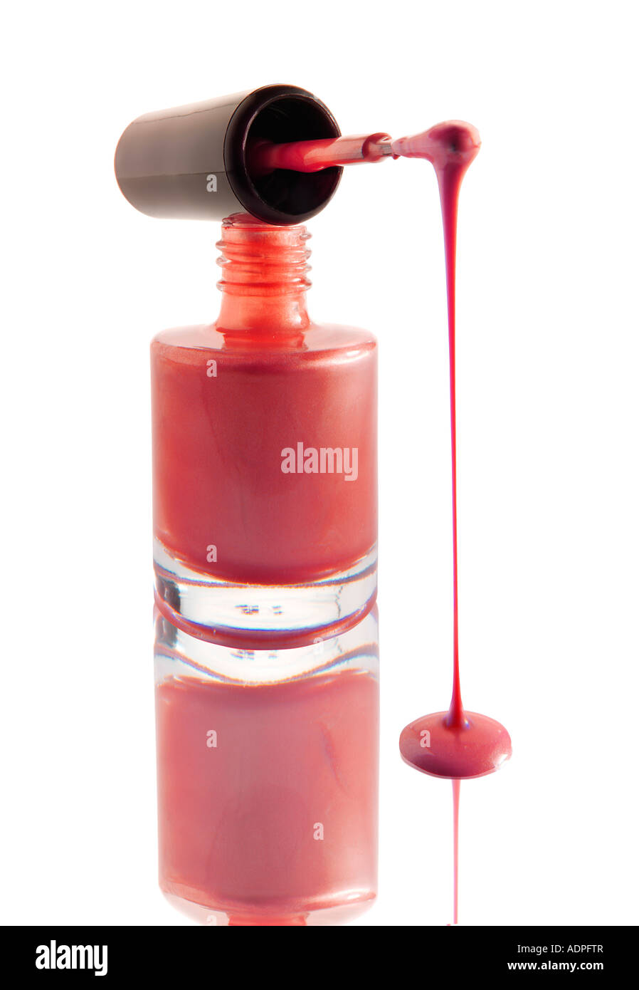 Smalto per unghie gocciolare da un smalto per unghie Spazzolino equilibrata su un chiodo del vaso di vernice rosa contro di colore bianco con una riflessione Foto Stock