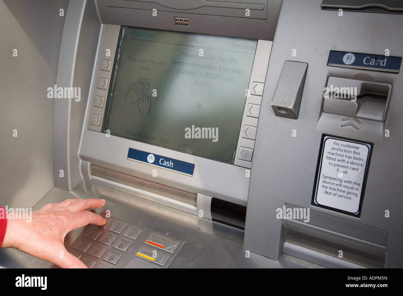 Foro nella parete ATM cash point machine auto teller immettere pin schermo con persona toccando i tasti pin al di fuori di una banca. Inghilterra Regno Unito Gran Bretagna Foto Stock