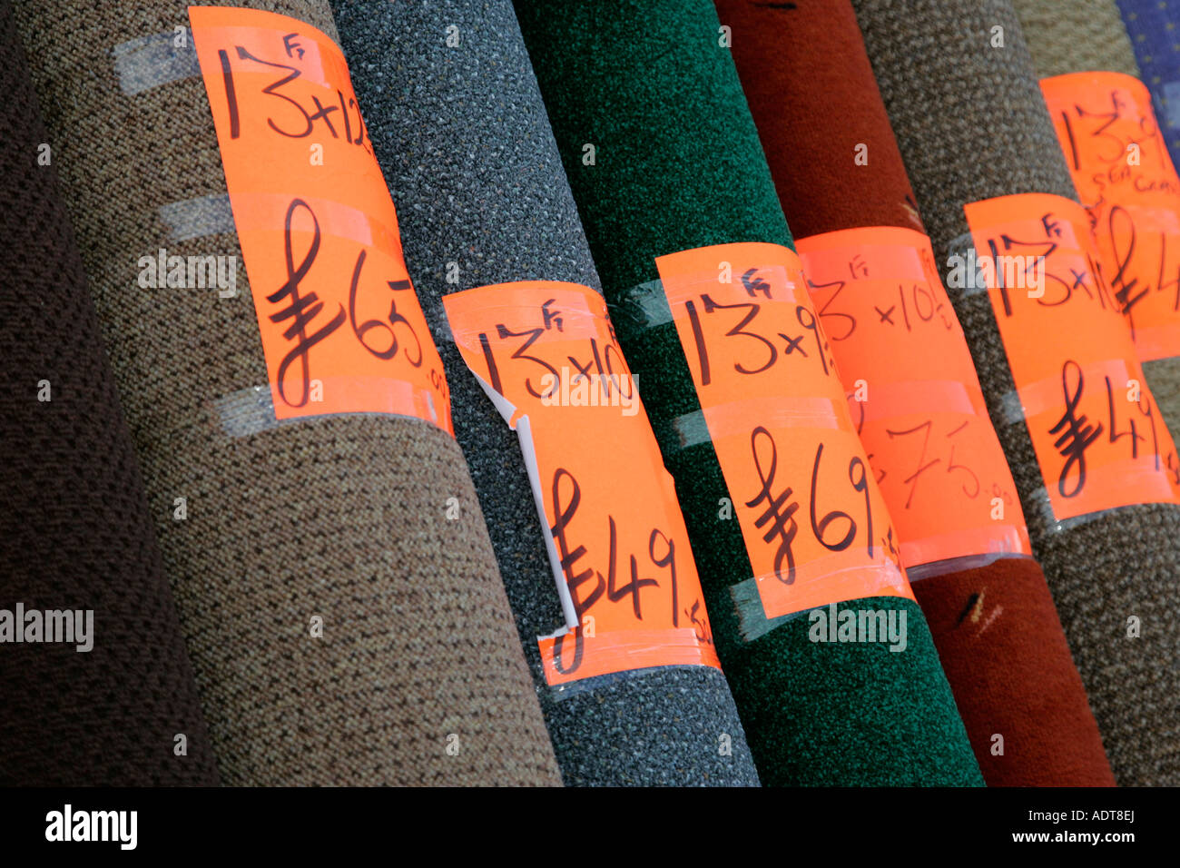 Rotoli di tappeto di uso domestico impilati sul display al di fuori di un negozio di tappeti con le etichette dei prezzi in sterline e misure imperiali Foto Stock