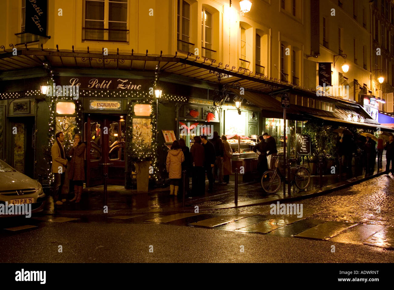 Persone rifugiate nella notte da pioggia su angolo di strada e leggere al di fuori del menu Le Petit Zinc ristorante Riva Sinistra di Parigi Francia Foto Stock