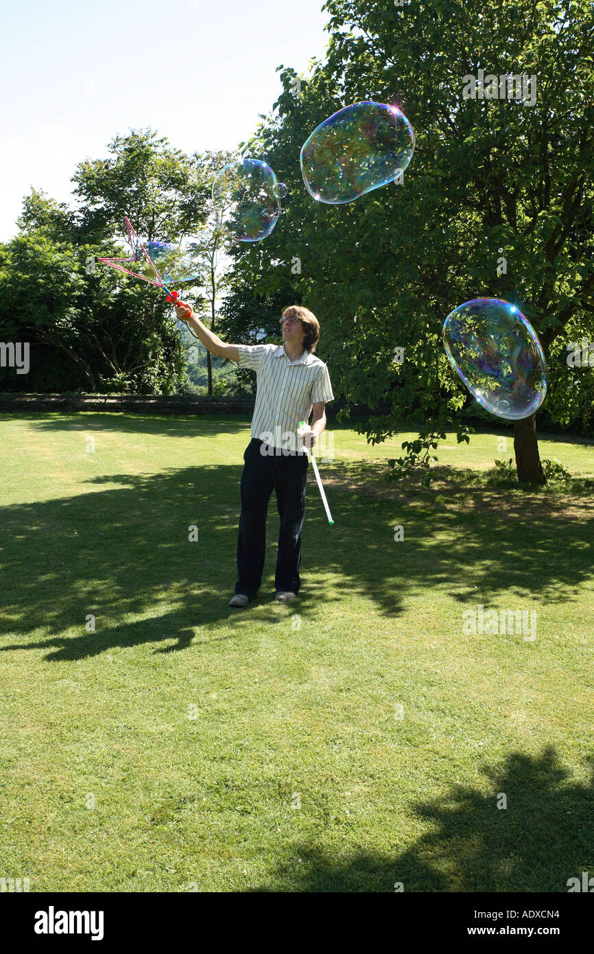 Giovane uomo utilizzando una bacchetta di bolla a creare enormi bolle. Su un prato in un giardino inglese. Foto Stock