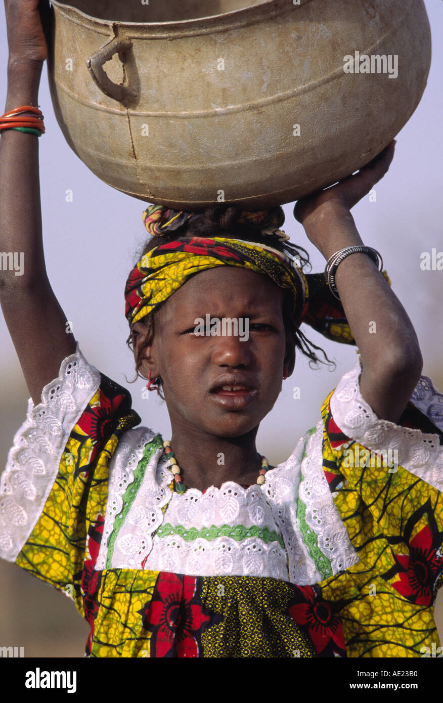 Ragazza Dogon equilibra una grande pentola di metallo sul suo capo Foto Stock