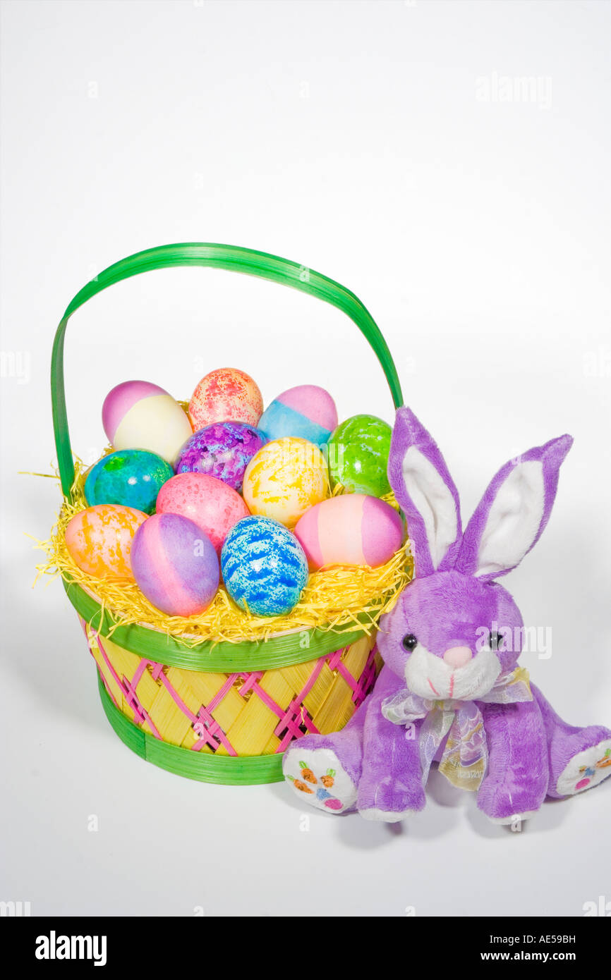La paglia Pasqua cesto pieno di uova di diversi colori e modelli con viola coniglietto ripiene Foto Stock