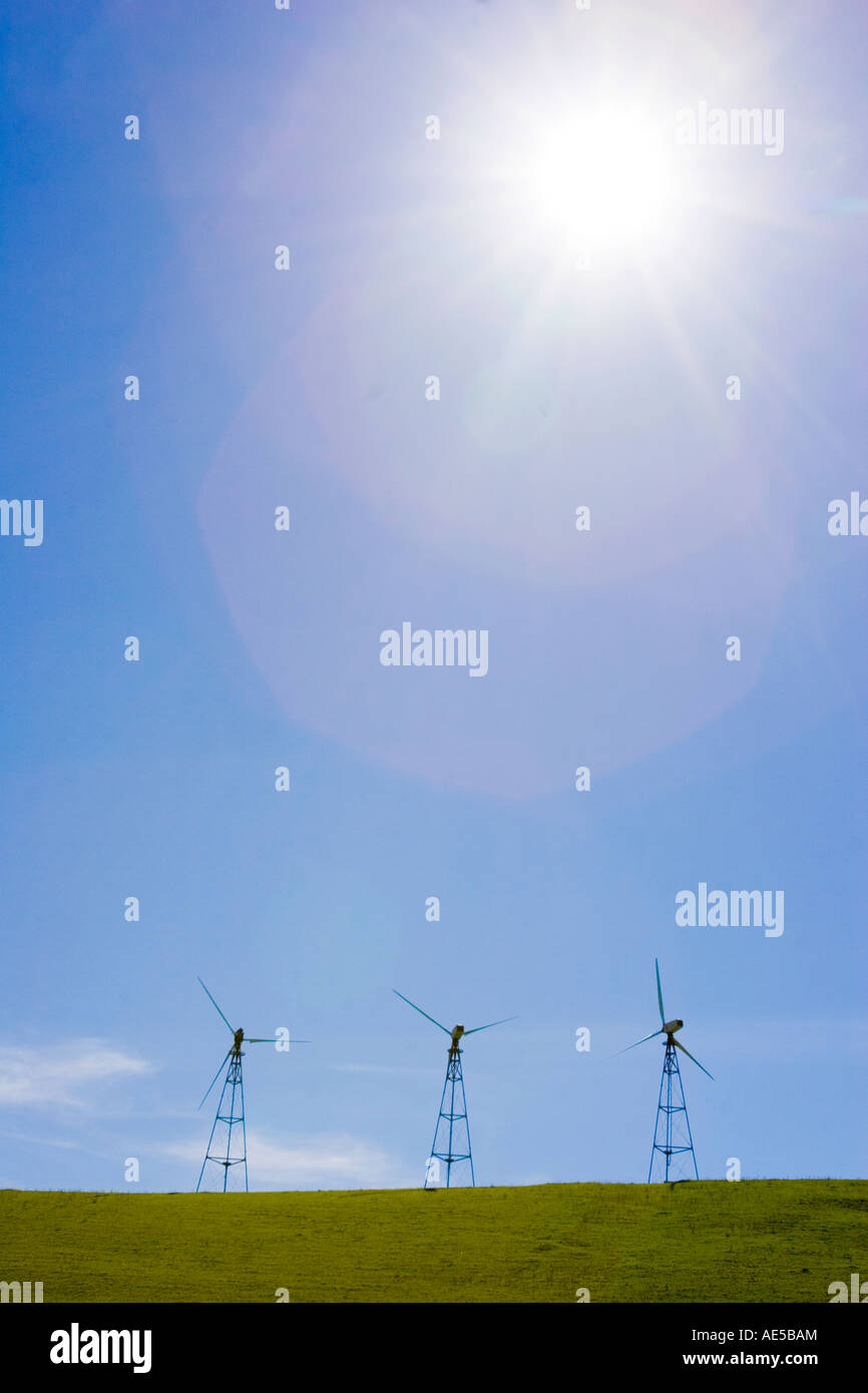 Sole che splende su tre mulini a vento sulla collina erbosa che mostra due tipi alternativi di fonti rinnovabili di energia eolica e solare Foto Stock