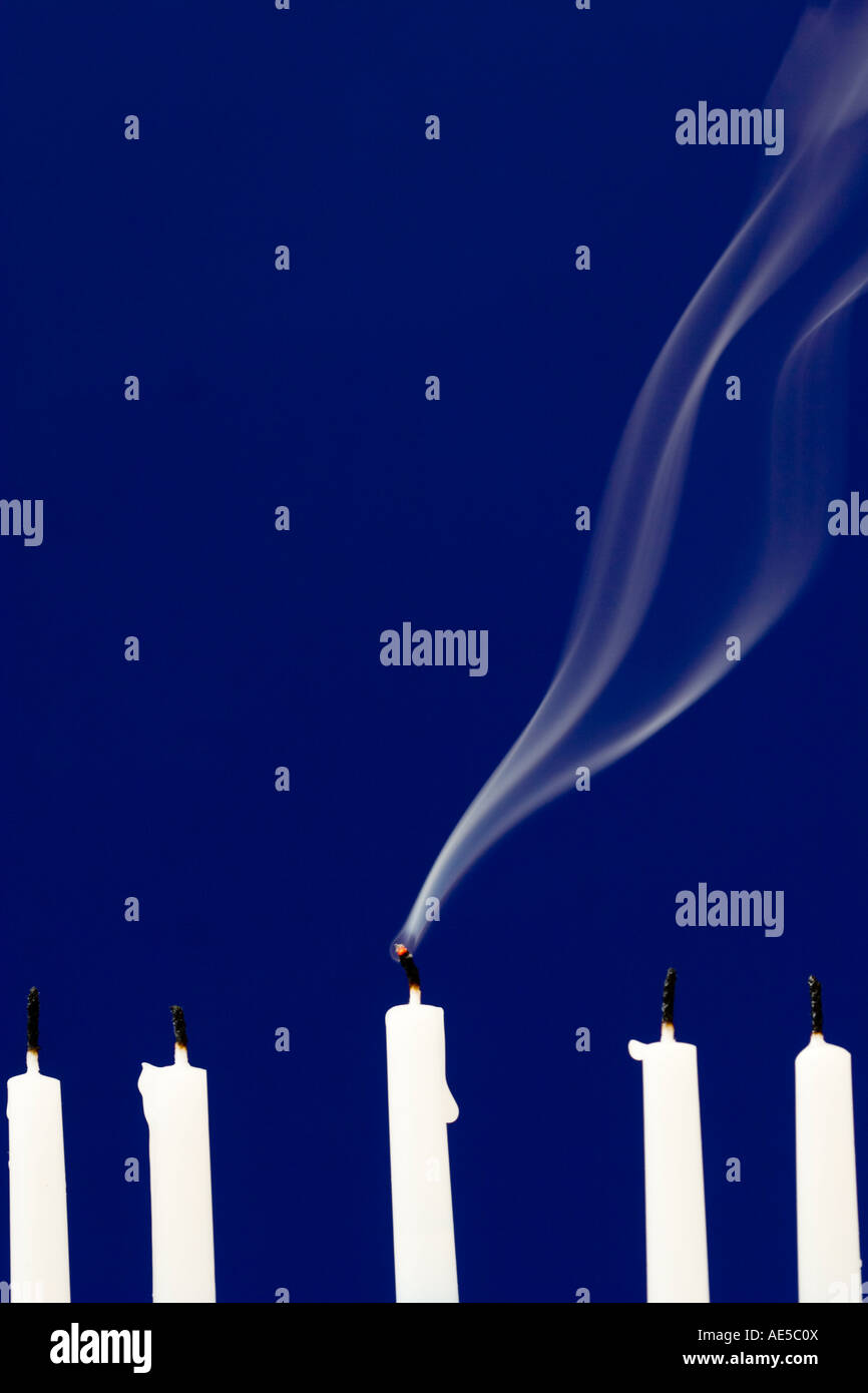 Cinque candele bianche che sono state soffiate con fumo che sale dal centro candela su sfondo blu Foto Stock