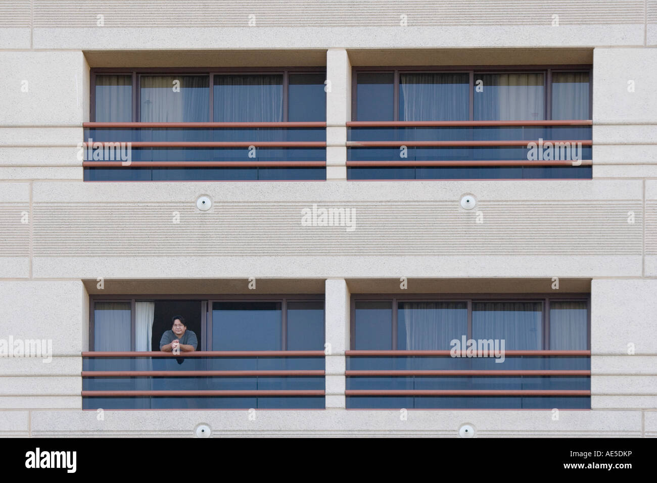 Americano cinese uomo età 40 appoggiata sulla ringhiera e guardando fuori da uno dei quattro hotel balconi in camera Foto Stock