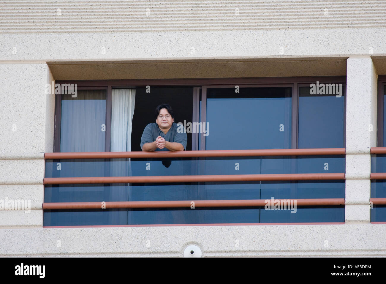 Americano cinese uomo età 40 appoggiata sulla ringhiera e guardando fuori da una stanza di un hotel balcone Foto Stock
