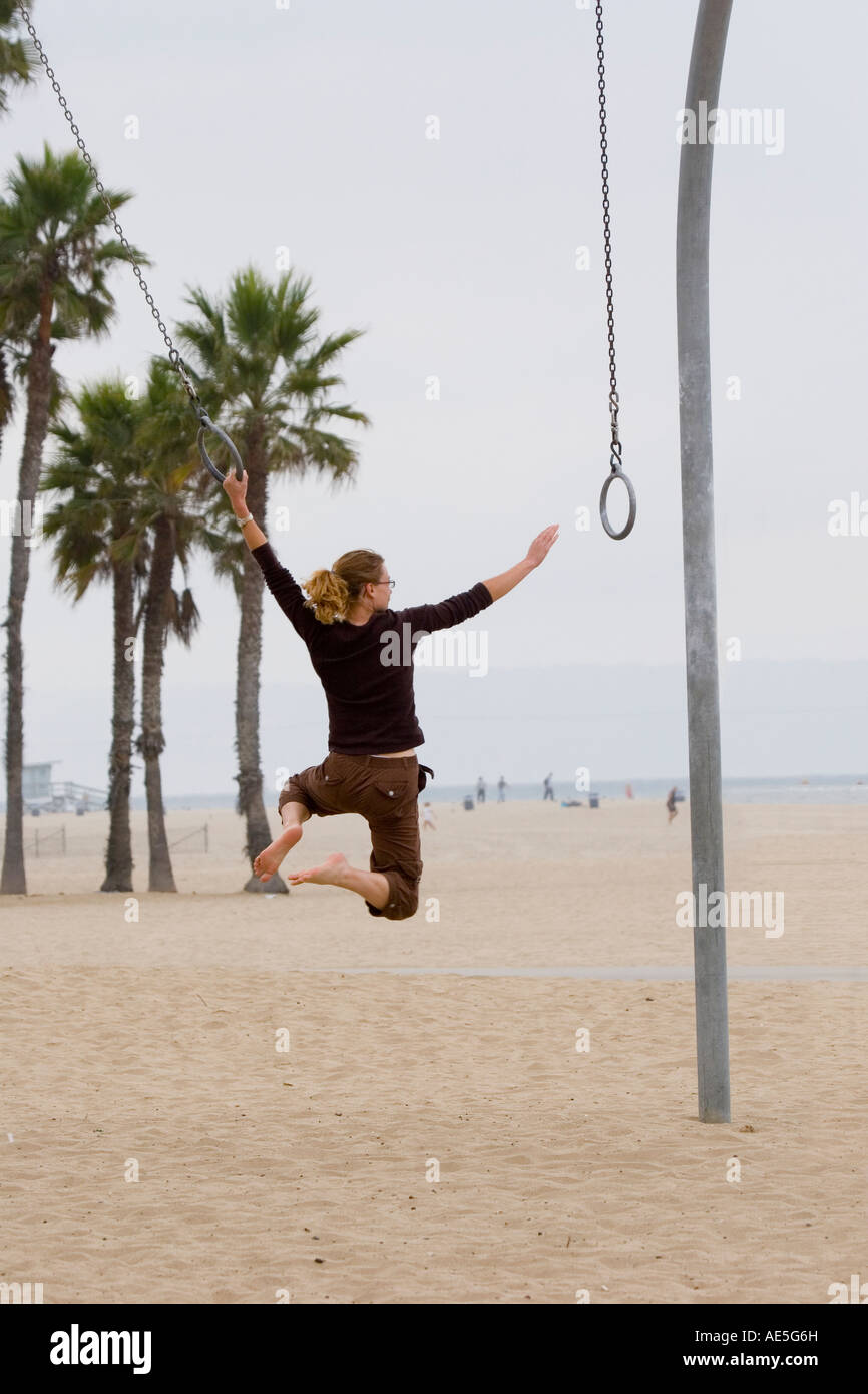 Donna raggiungendo per la successiva oscillazione ad anello sul set di anelli sulla spiaggia di Santa Monica a Los Angeles, California. Foto Stock