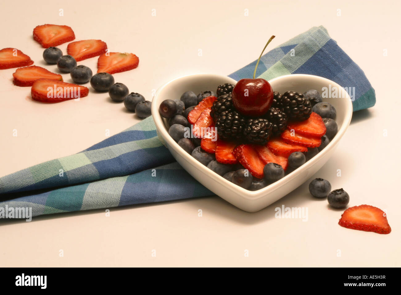 Cuore con freccia fatta di frutti di bosco freschi in un cuore piatto e tovagliolo a scacchi Foto Stock