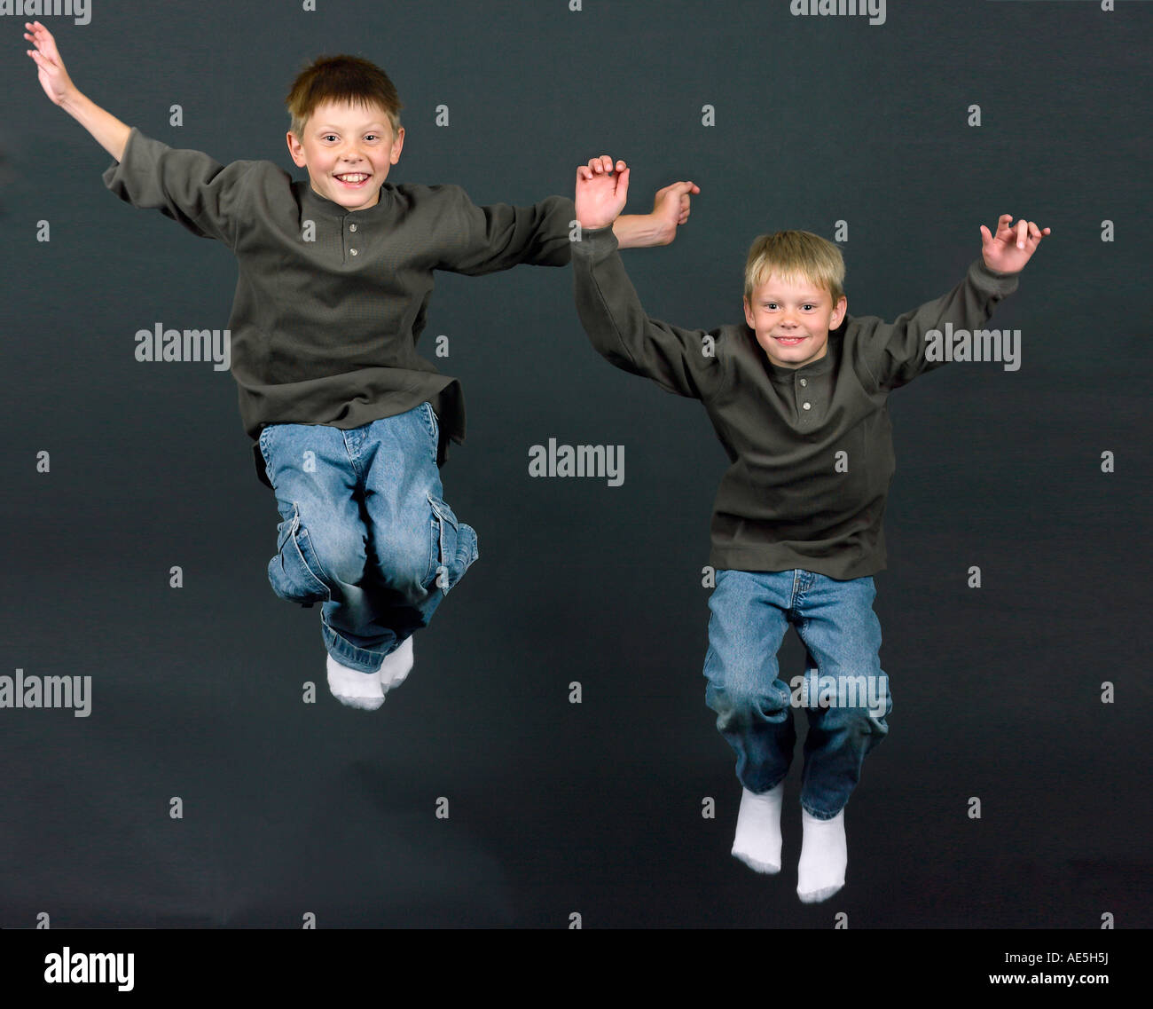 Due fratelli bionda in corrispondenza di jeans e henley shirts il salto in aria per la gioia Foto Stock