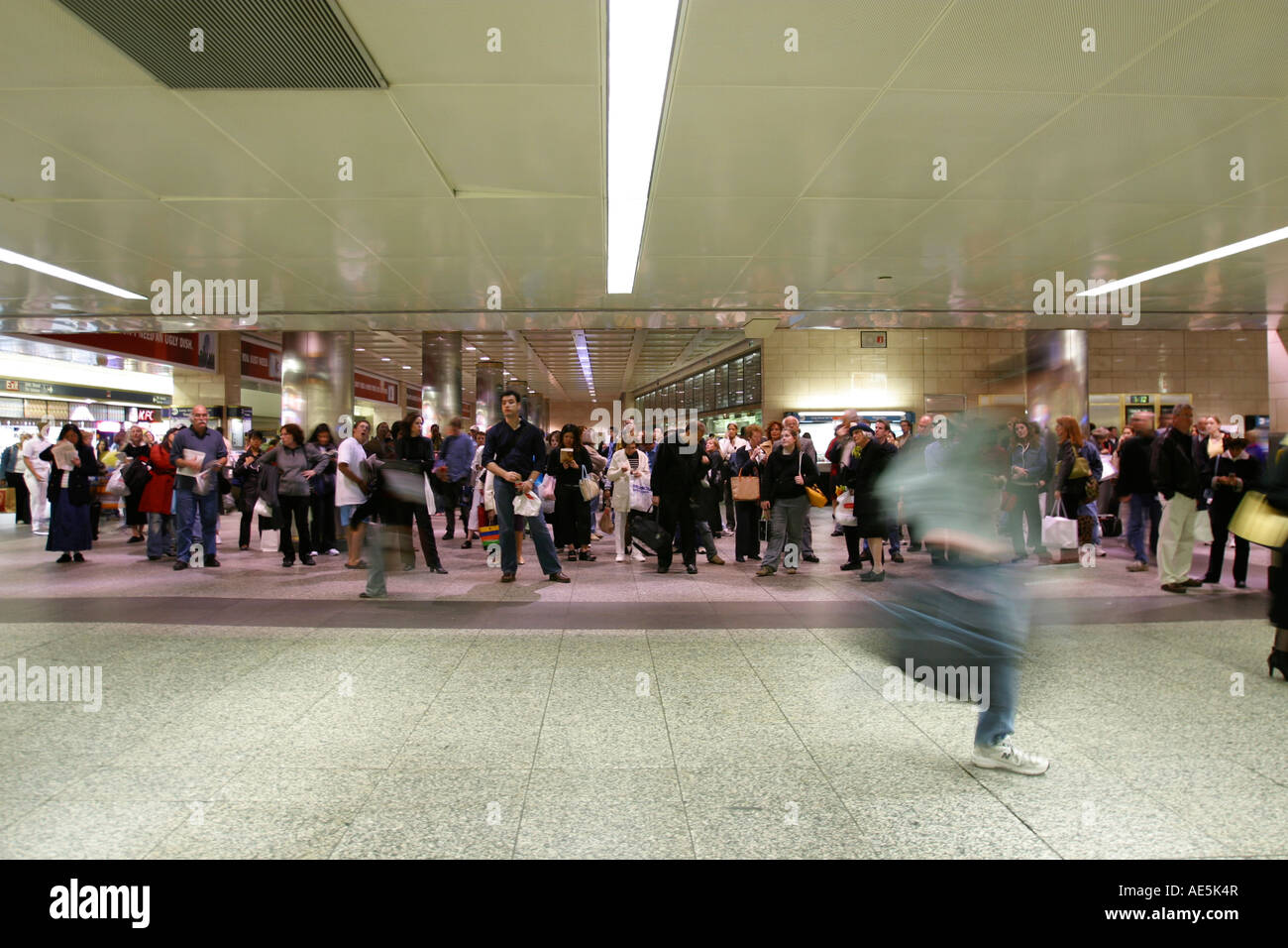 Le persone in piedi in un'area di attesa di Penn Station guardando il treno la pianificazione come uomo precipita da per catturare il suo treno Foto Stock