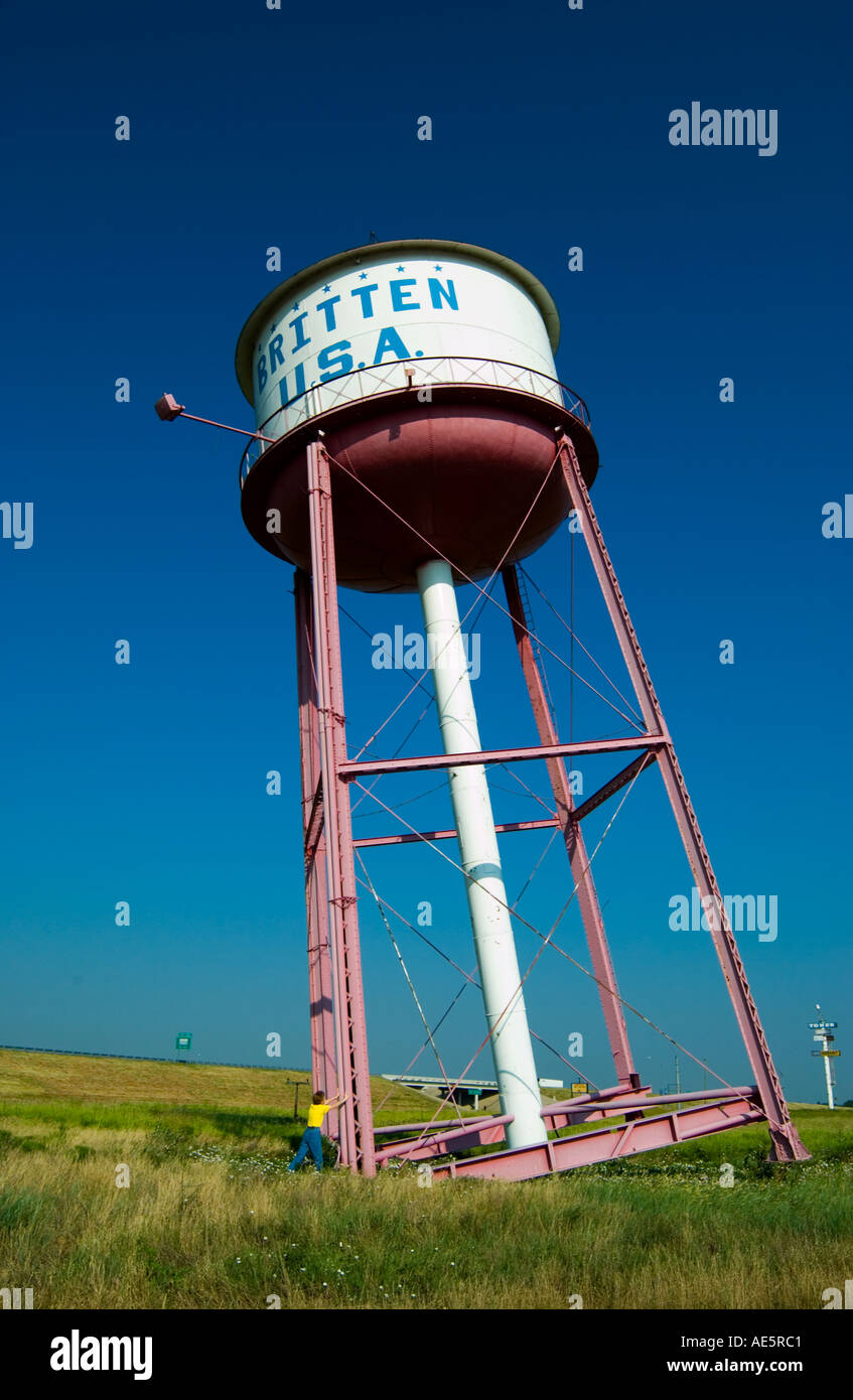 Donna caucasica che si posa umoristicamente come se avesse in mano la torre dell'acqua inclinata a Britten, Texas, USA. Foto Stock