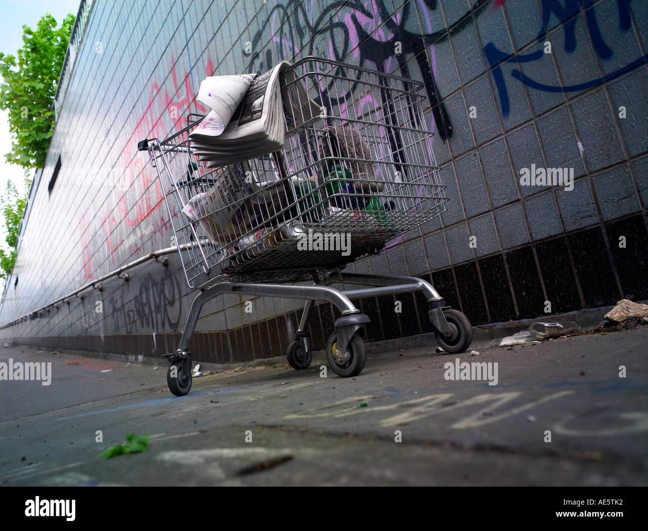 Carrello trolley utilizzato da persona senza dimora su un sottopassaggio di Manchester con graffitti sulla parete Foto Stock