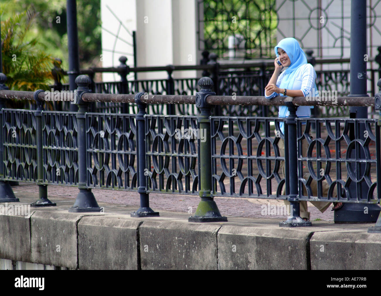 Ragazzina musulmana del coperchio che indossa una testina del blu sciarpa, utilizzando un telefono cellulare, Riverfront, Sungai Fiume Sarawak Kuching, Borneo Malaysia Foto Stock