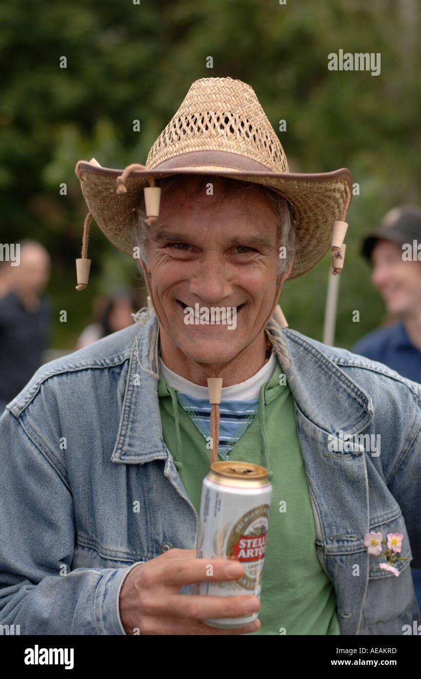 Uomo sorridente nel suo 40s può bere di lager indossando hat con tappi di sughero penzolanti da esso Foto Stock
