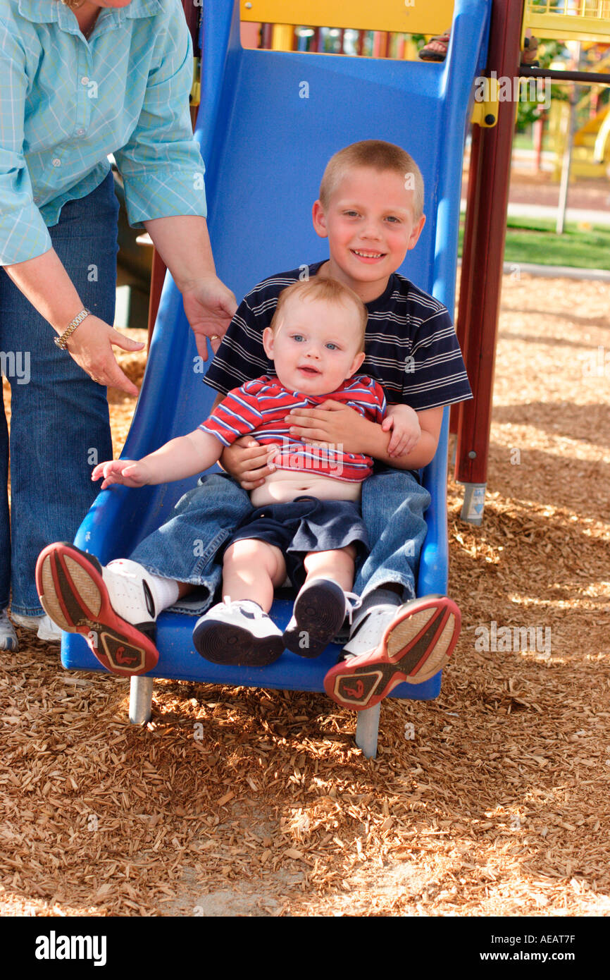 5 anno vecchio ragazzo azienda 1 anno di età bambino sul parco giochi slitta Foto Stock