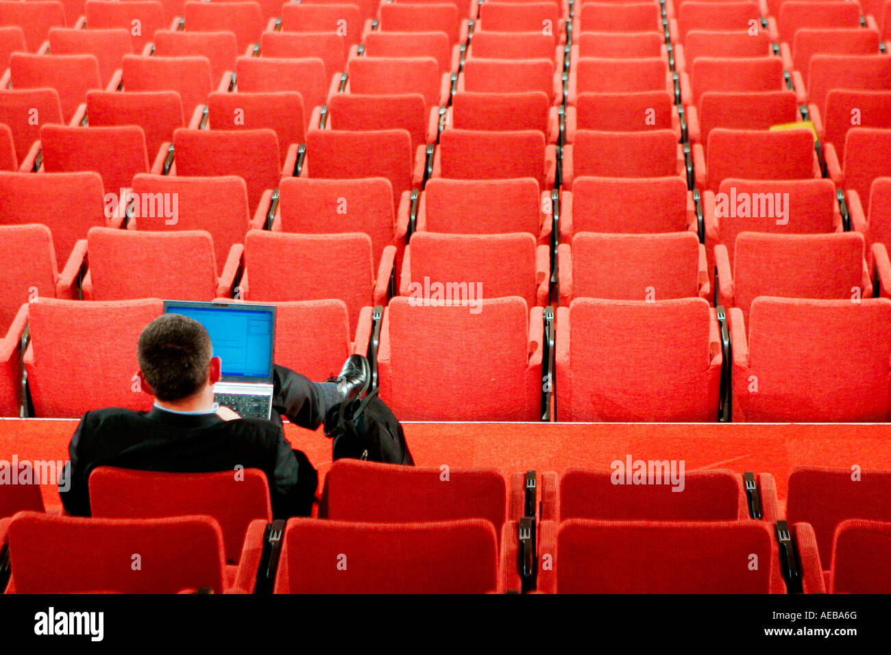 Uomo solitario con un lap top seduto in una stanza con sedie rosse Foto Stock