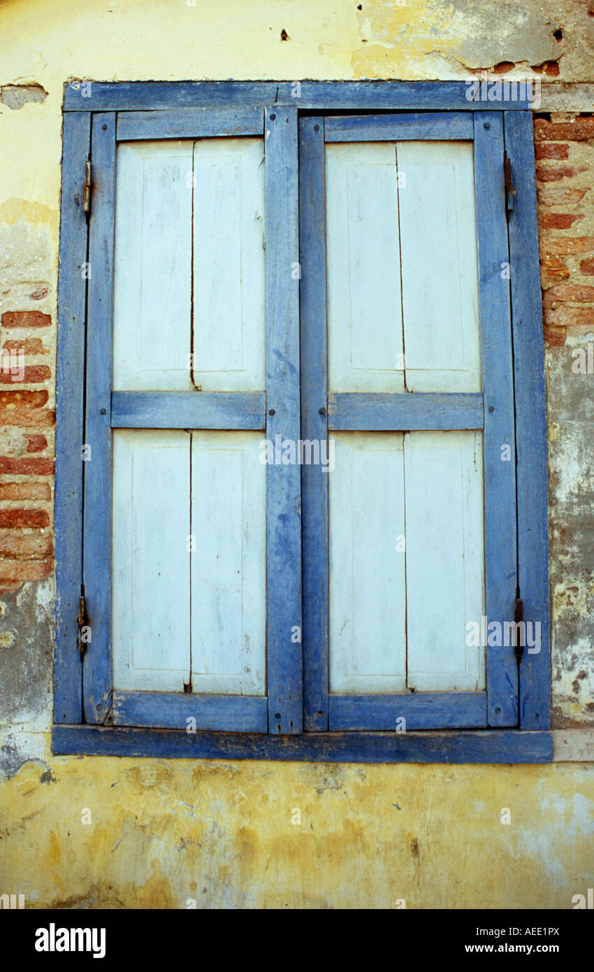 Chiuso il blu dipinto di persiane in legno in weathered decadendo francese antico edificio coloniale, Kampot, Cambogia Foto Stock