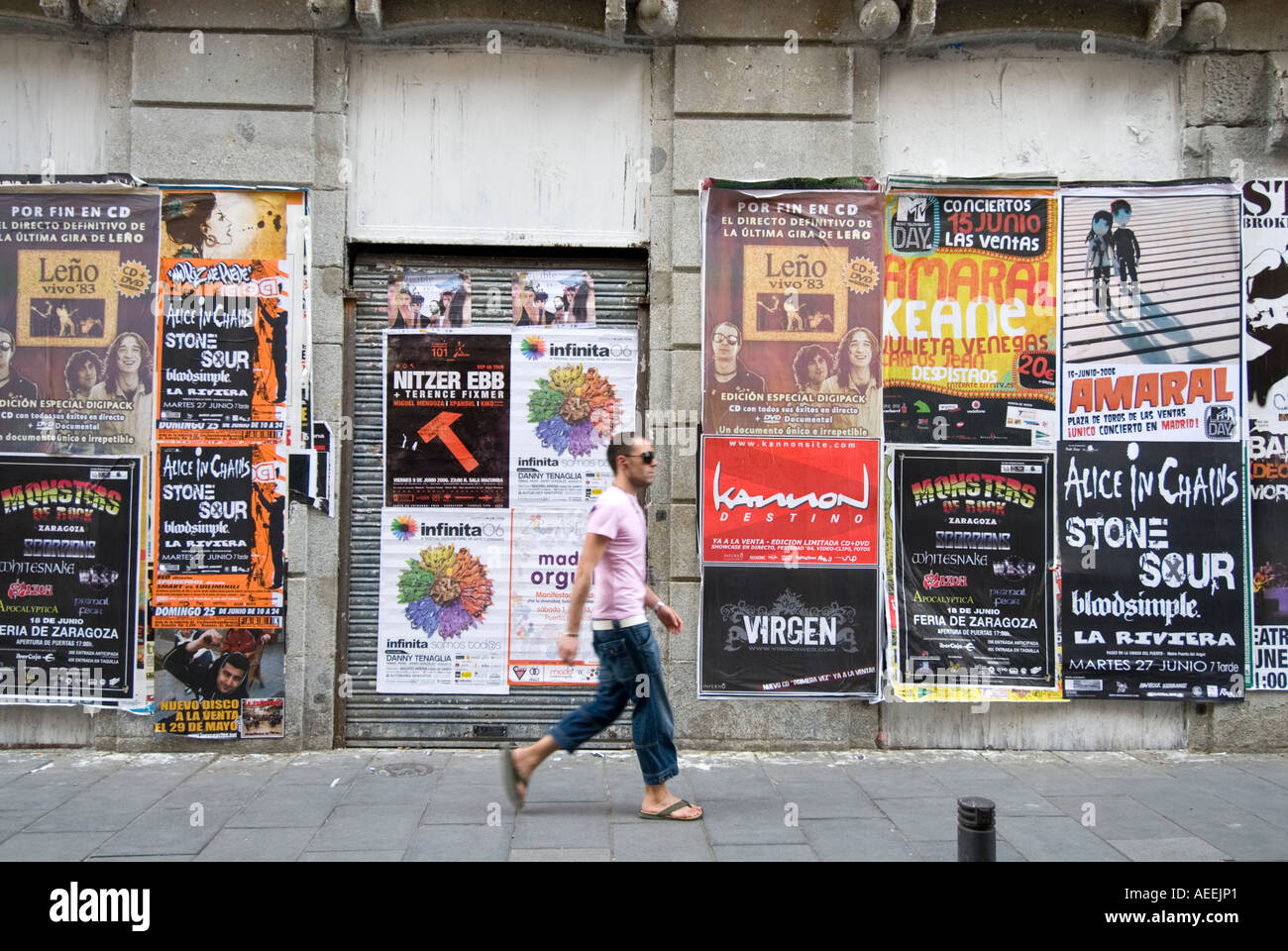 Uomo che cammina passato volare poster pubblicitari bande rock in zona Chueca, Madrid Spagna Foto Stock