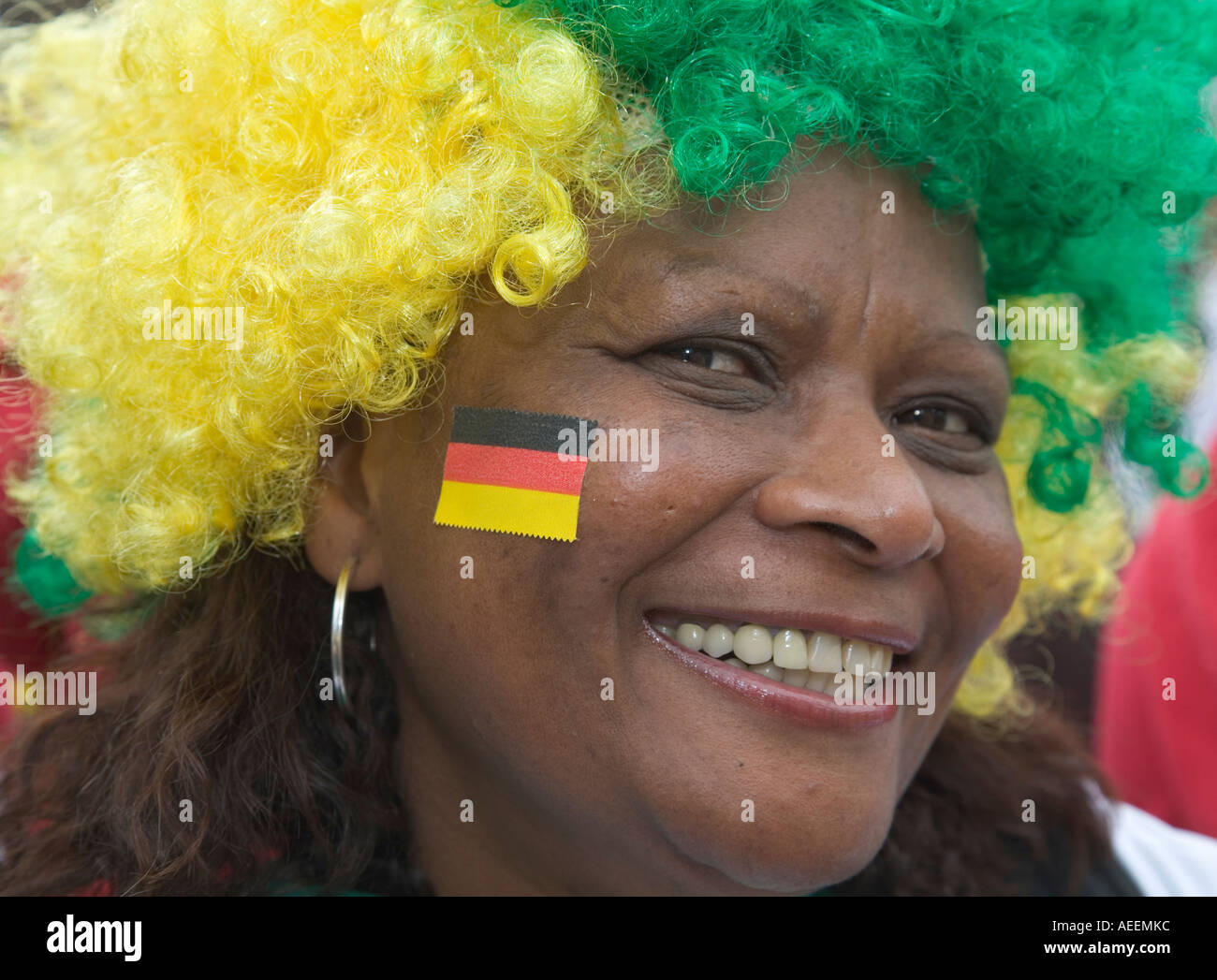 Una femmina di fan del calcio brasiliano squadra indossa una parrucca nei suoi colori nazionali e ha una piccola bandiera tedesca incollata sulla sua guancia Foto Stock